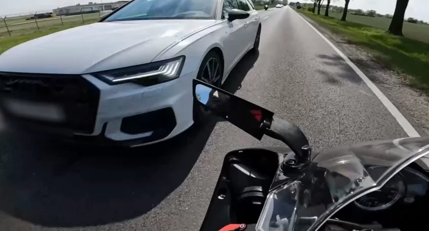 Kierujący samochodem marki Audi wyprzedza „na trzeciego”, zmuszając motocyklistę  do gwałtownego manewru celem uniknięcia zderzenia