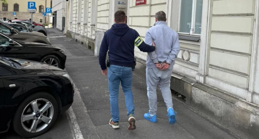 Podejrzany w kajdankach prowadzony przez funkcjonariusza Policji